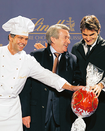 Ernst Tanner, Roger Federer und ein Maitre Chocolatier berühren eine große Lindor Kugel (Foto)