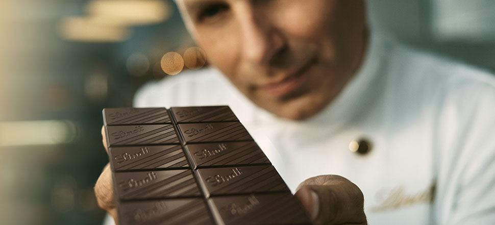 Ein Maître Chocolatier hält eine Tafel Schokolade in der Hand und reicht sie in die Kamera (Foto)