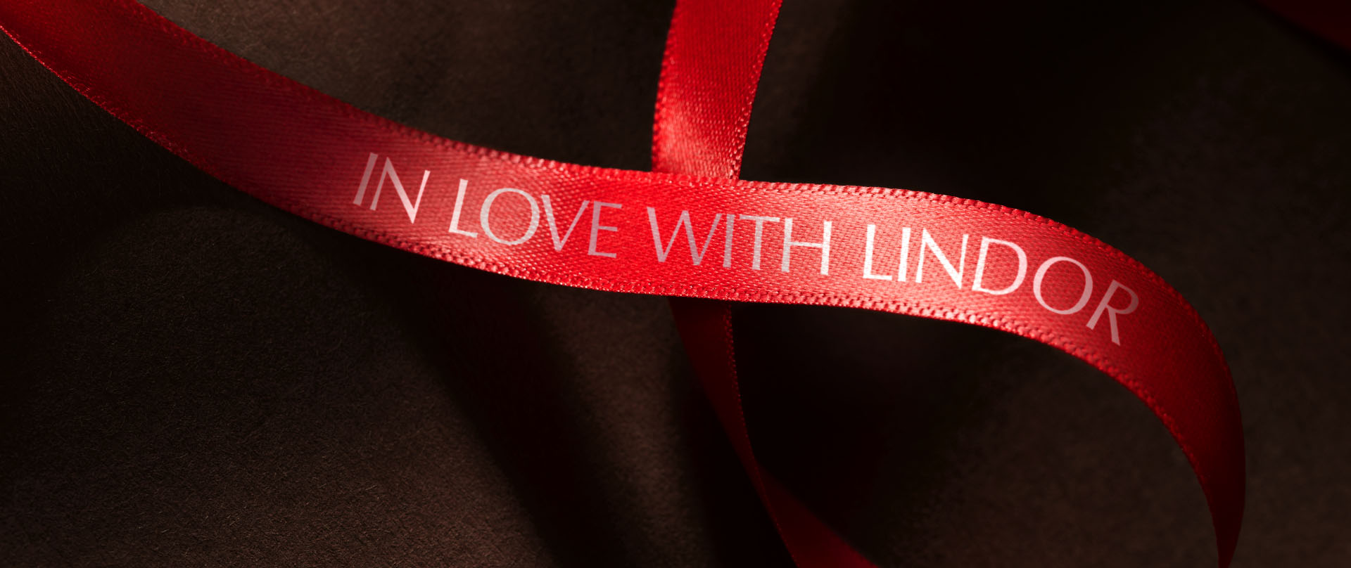 Eine rote Schleife mit der Aufschrift „In love with LINDOR“ auf einem braunen, seidenen Hintergrund (Foto)