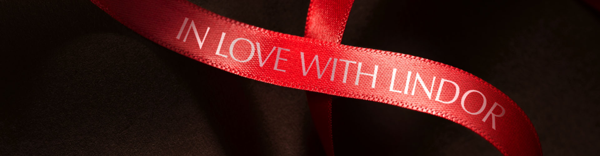 Eine rote Schleife mit der Aufschrift „In love with LINDOR“ auf einem braunen, seidenen Hintergrund (Foto)