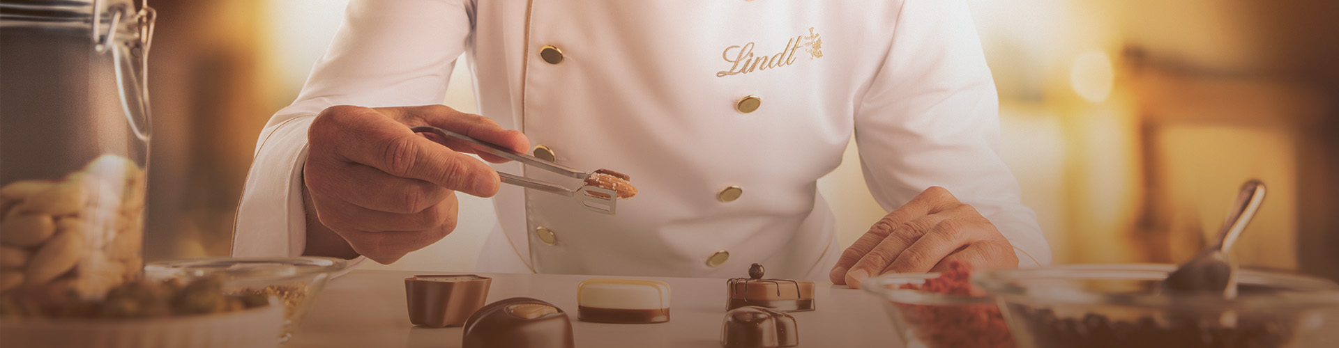 Maître chocolatier Urs Liechti dekoriert Pralinen und hält eine Mandel in einer Zange. (Foto)