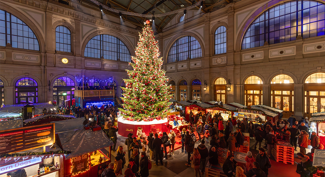 Christkindlmarkt im Zürcher Hauptbahnhof mit vielen Menschen versammelt um den Weihnachtsbaum (Foto)