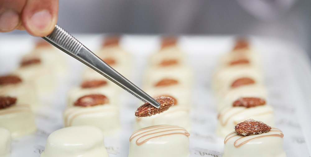 Precision placing of almonds on pralinés with pincers (Photo)