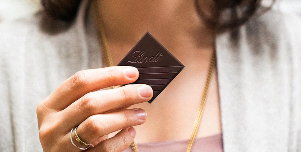 A square of Lindt chocolate held infront of person as if to eat (Photo)