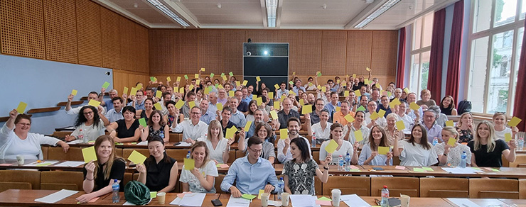 People in an auditorium holding up large yellow sticky notes (Photo)